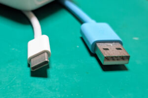 白いUSB Type-Cコネクタと青いUSB Type-Aコネクタが並んで置かれている様子。緑色の背景上で撮影されており、それぞれの端子形状の違いが視覚的にわかりやすく示されている。